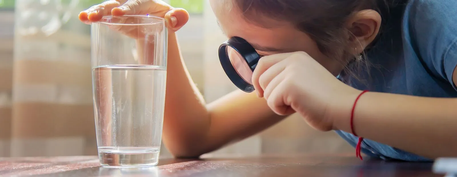 The child examines the water with a magnifying glass in a glass. Selective focus..jpg